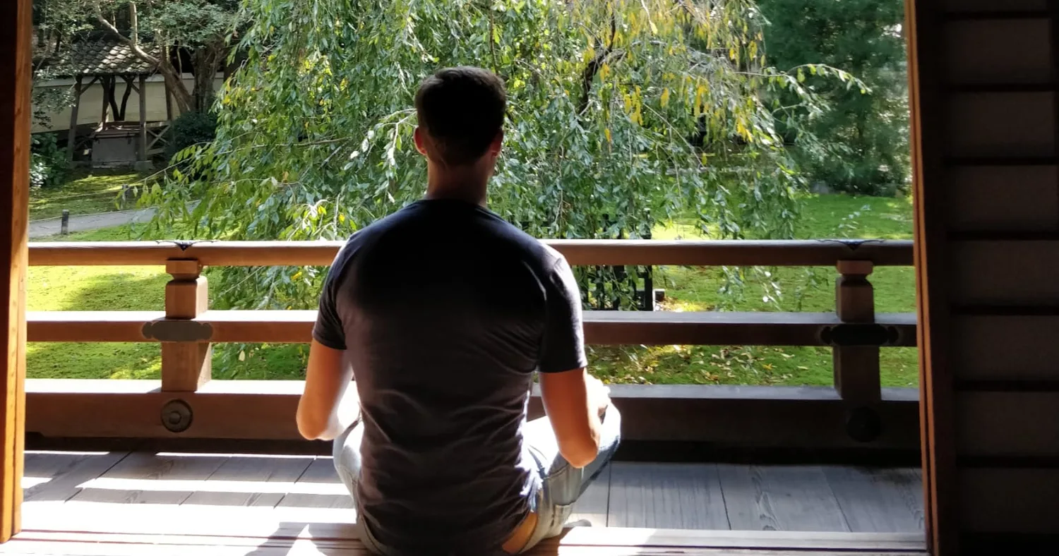 Médéric zit in meditatie op een houten veranda met uitzicht op een groene tuin