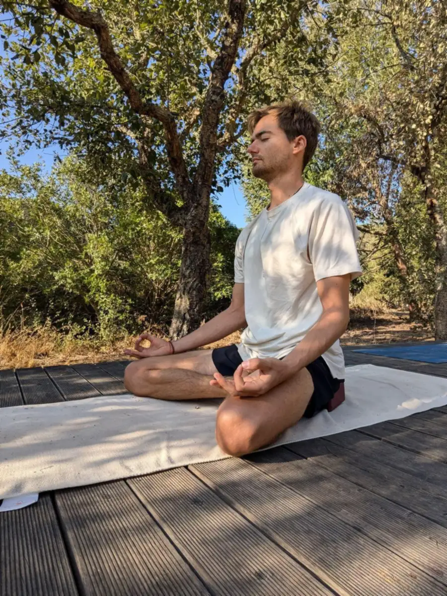 Mederic mediteert buiten op een yogamat onder de bomen